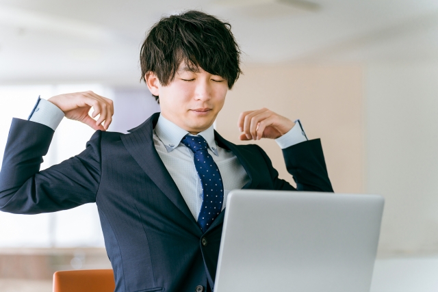 デスクで腕を上げて肩を押さえるスーツ姿の男性