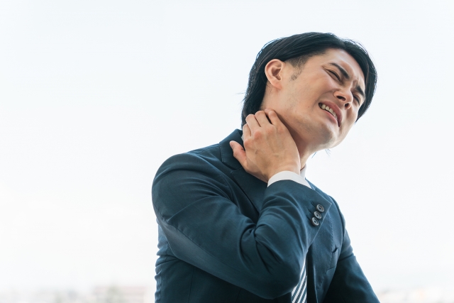 窓辺で首の後ろを押さえる男性
