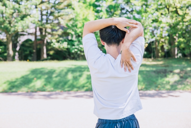 屋外で腕を頭の後ろに回してストレッチする男性