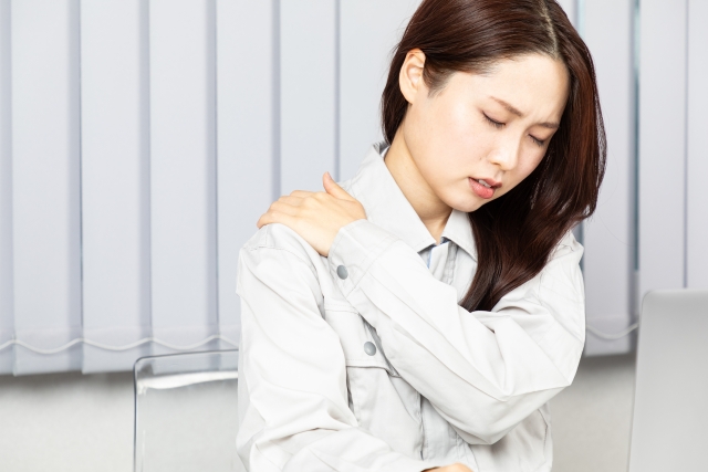 腕を組んで肩を押さえる女性